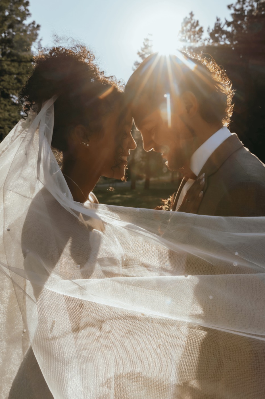 Couple forehead to forehead at sunset, wrapped in the bride's flowing veil